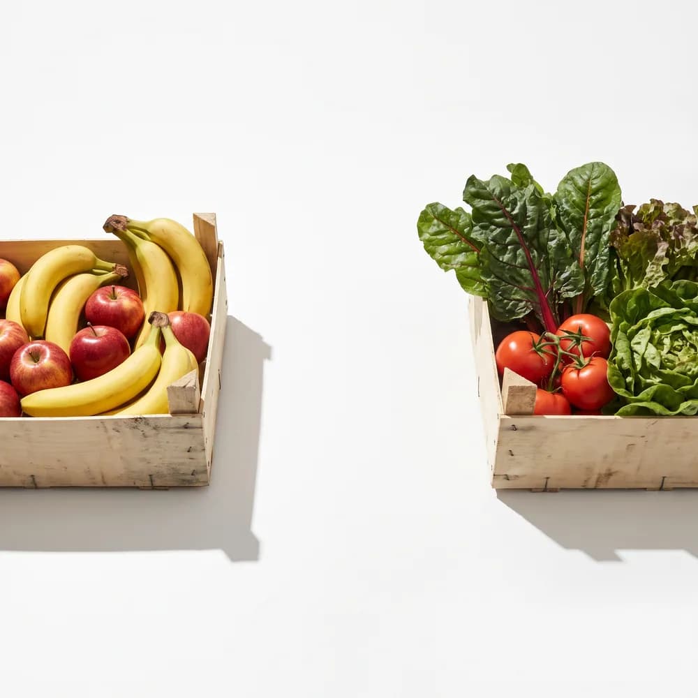 Plátanos y manzanas en una caja y, apartada, otra caja con jitomate y hojas verdes.