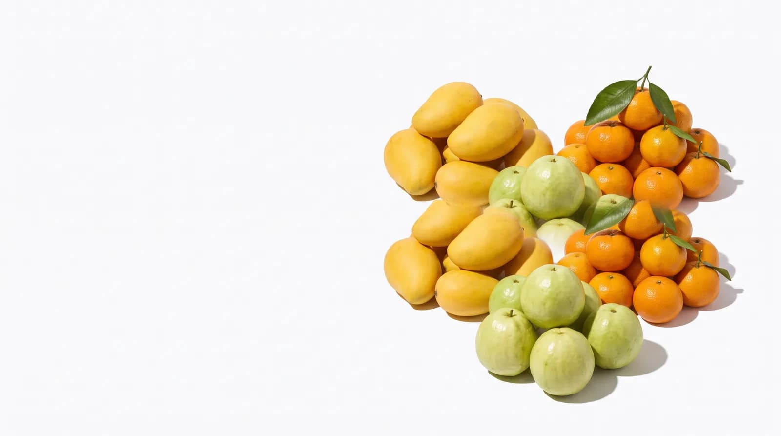 Tres montones de fruta de temporada sobre una mesa blanca: mango, guayaba y mandarina.